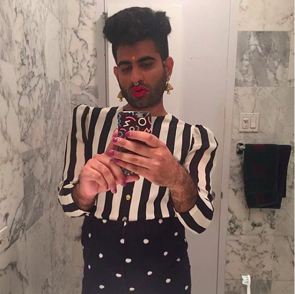 Alok taking selfie in a black and white marbled bathroom, donning a black polka dotted skirt, white striped blouse, a bindi, purple nail polish, and red lipstick.